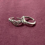 Flat lay image of V-Shape Filigree Tiara Toe Rings on maroon background