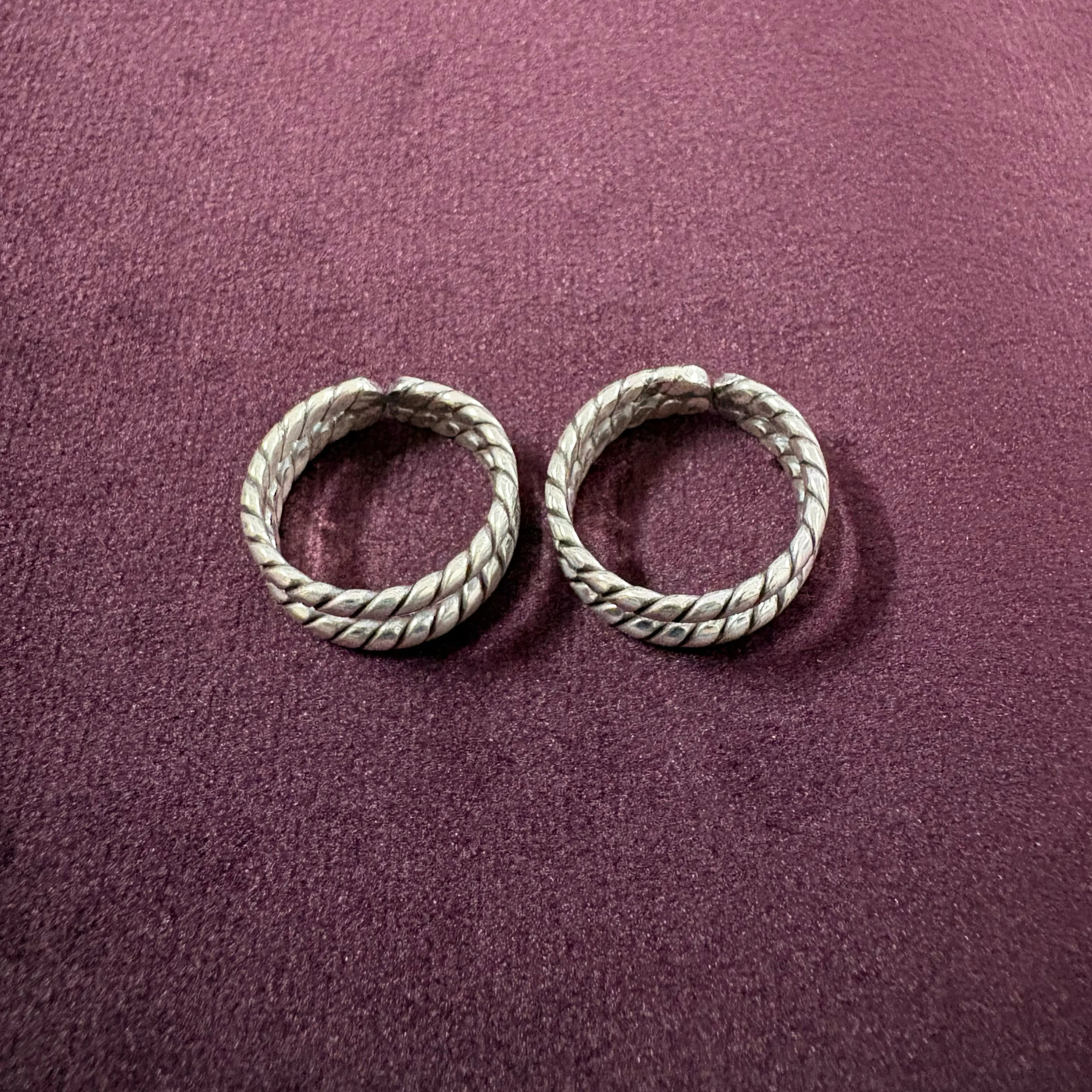 Flat lay image of Twisted Double-Rope Oxidized Toe Rings on maroon background