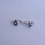 Silver toe rings with blue and white evil eye design on a solid background