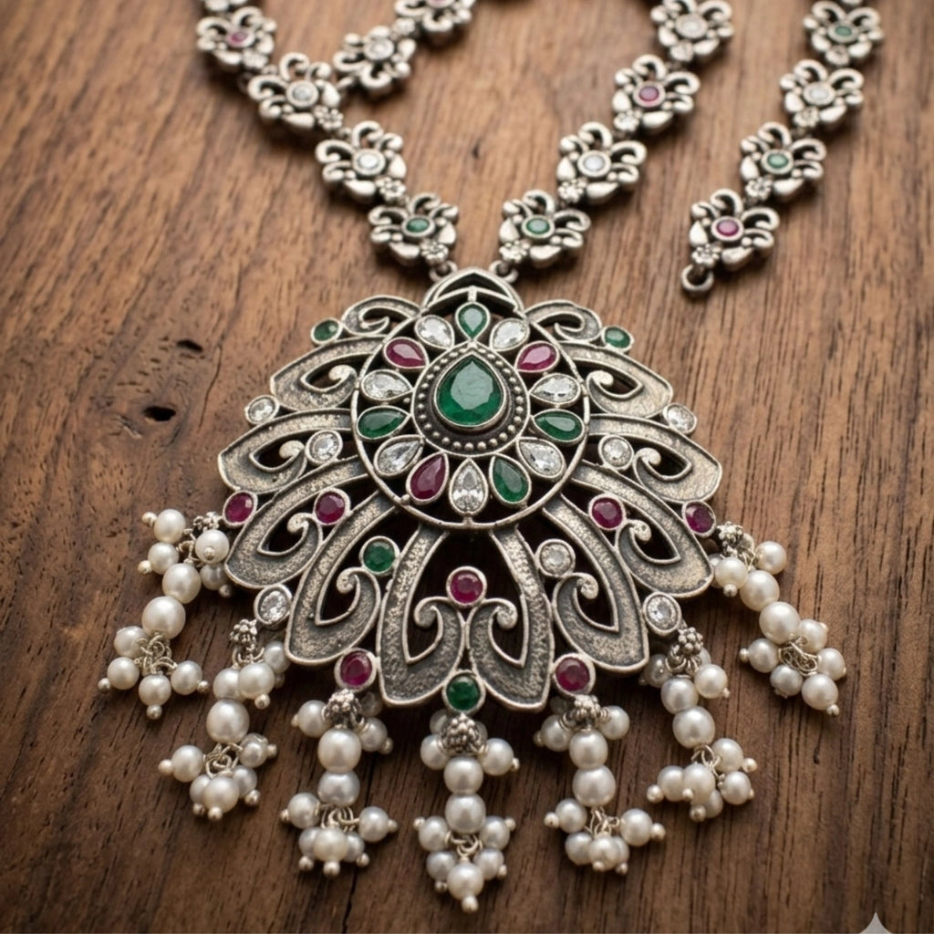 Ornate silver necklace with pearls and gemstones on a wooden surface
