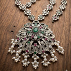 Ornate silver necklace with pearls and gemstones on a wooden surface