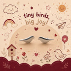 A pair of small silver bird-shaped earrings displayed on a beige background with a whimsical doodle-style illustration featuring a rainbow, sun, clouds, birdhouse, and the text 'tiny birds, big joy!'.