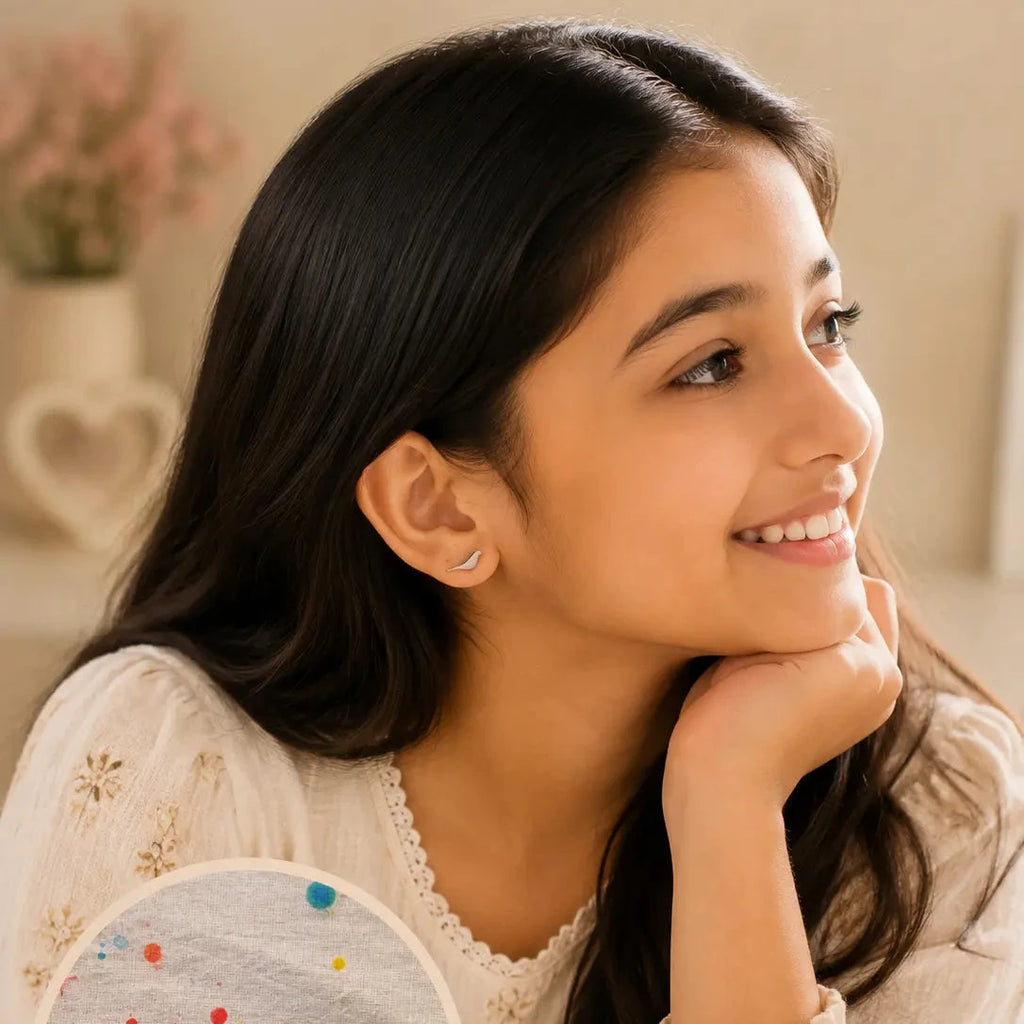 A young girl with long dark hair is shown in a warm indoor setting, wearing small bird-shaped stud earrings. A circular inset highlights the earrings, which feature silver-toned birds with colorful dot accents on a light background.