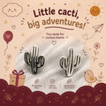 Cactus-shaped stud earrings displayed on a white textured surface inside a decorative illustrated card. The card reads 'Little cactus, big adventures!' and includes text noting 92.5 sterling silver.