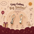 A pair of tiny sterling silver cube-shaped dangle earrings displayed on a decorative beige and burgundy card. The card features cute cartoon illustrations of a sun, cloud, bird, gift box, and stars, along with text that reads 'Tiny Cubes, Big Smiles!' and '92.