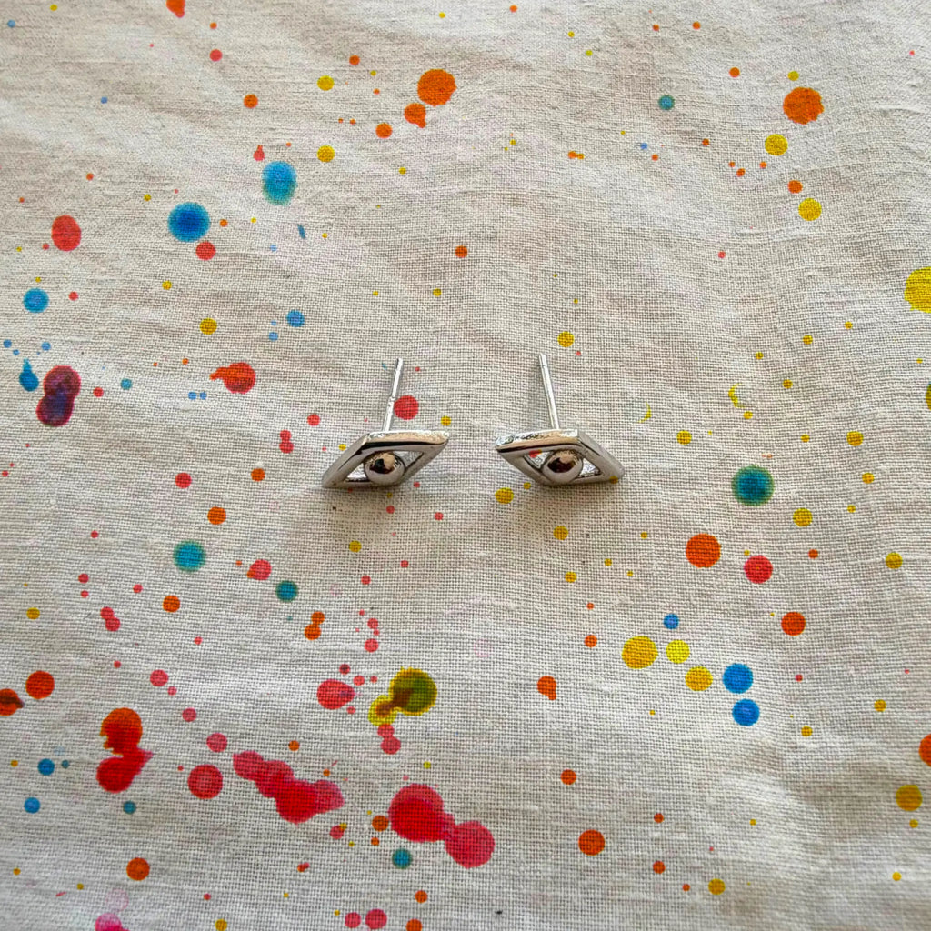 Evil Eye Earrings with color splattered on beige fabric