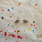 Evil Eye Earrings with color splattered on beige fabric