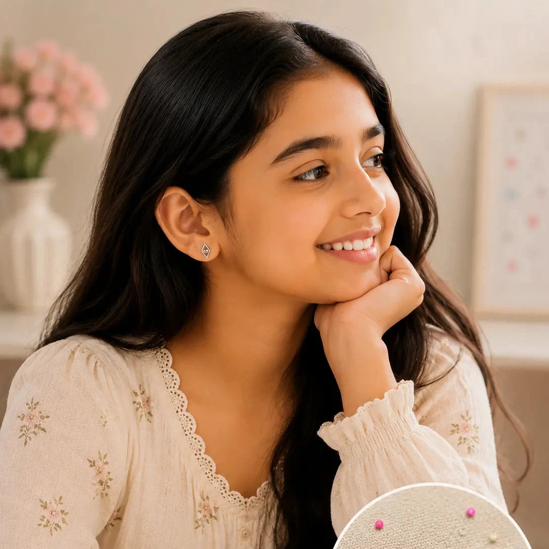 A young girl with long dark hair is smiling and looking to the side, wearing a cream floral blouse. In the lower right, an inset circle shows a pair of silver geometric stud earrings with small colorful bead details pinned onto fabric.