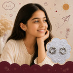 A young girl with long dark hair smiles while wearing a small silver intertwined Star stud earring. An inset cloud graphic on the right shows a pair of silver Star of David earrings on a textured gray background.