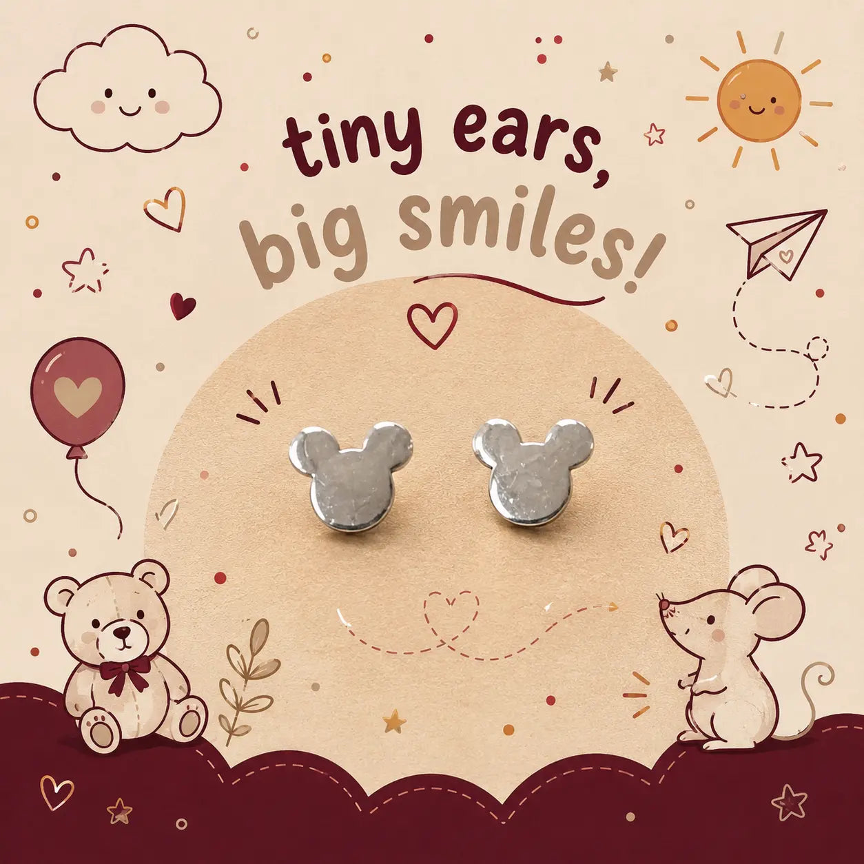 A pair of small silver stud earrings shaped like mouse ears, displayed on a beige card with cute teddy bear, mouse, sun, and cloud illustrations. The card reads 'tiny ears, big smiles!'.