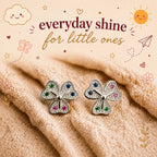 A pair of silver petal-shaped stud earrings with small multicolored gemstones, displayed on a soft beige textured blanket with decorative text and doodles reading 'everyday shine for little ones'.