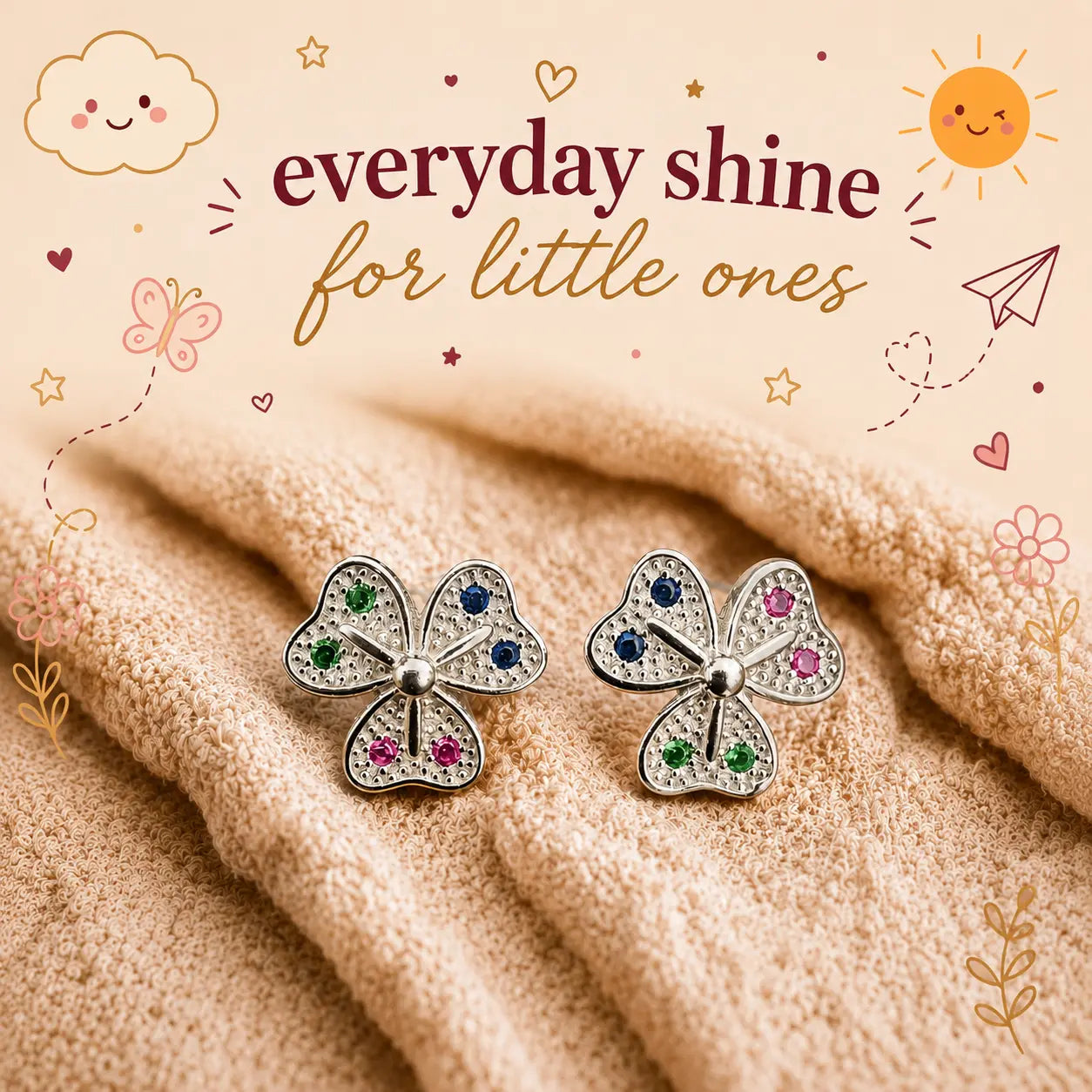 A pair of silver petal-shaped stud earrings with small multicolored gemstones, displayed on a soft beige textured blanket with decorative text and doodles reading 'everyday shine for little ones'.