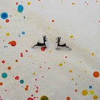 A pair of small silver deer stud earrings with black enamel detailing, displayed on a textured off-white fabric with colorful paint splatters.