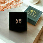 A pair of small fawn stud earrings in 925 sterling silver, displayed on a black velvet jewelry box next to its green branded packaging box. The setting is on a light marble surface with a soft-focus background.