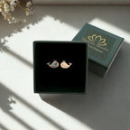 A pair of whale-shaped stud earrings displayed in an open dark green jewelry box, with the branded box lid placed behind it on a softly lit surface.